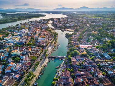 Hoi An 'ın hava aracı görüntüsü. Vietnam' ın dolambaçlı nehri, çatıları ve günbatımında uzak tepeleri olan bir kasabası. Seyahat blogları, turizm pazarlaması ve editoryal özellikler için mükemmel..