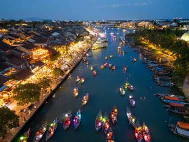 Gece vakti fener festivali sırasında Hoi An, Vietnam 'ın çarpıcı hava fotoğrafı. Parlayan sokak ışıkları ve kalabalık eski kasabayı canlandırırken renkli tekneler nehirde yüzüyor..