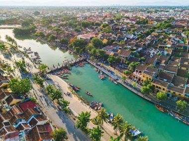 Geleneksel çatılar, turkuaz nehir ve renkli teknelerin yer aldığı Hoi An, Vietnam manzaralı. Seyahat reklamları, kültür makaleleri ya da turizm afişleri için ideal. Yüksek kalite görsel.