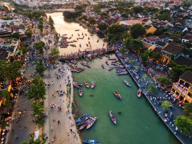 Gün batımında Hoi An, Vietnam 'ın canlı hava manzarasında tarihi bir köprüde fener botları ve hareketli kalabalıklar görülüyor. Turizm reklamları, editoryal içerik ve kültürel hedef pazarlama için ideal.