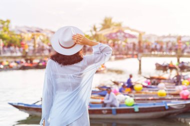 Beyazlı bir kadının şapkasını tutarken Hoi An 'daki renkli fener teknelerine baktığı görüntüler Vietnam' da seyahat, yaşam tarzı ya da yayın tanıtımı için yüksek kaliteli, modaya uygun bir görüntü..