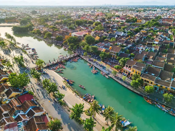 Geleneksel çatılar, turkuaz nehir ve renkli teknelerin yer aldığı Hoi An, Vietnam manzaralı. Seyahat reklamları, kültür makaleleri ya da turizm afişleri için ideal. Yüksek kalite görsel.