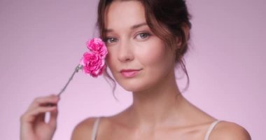 Yavaş çekim, zarif bir genç kadının pembe bir çiçek tutup yüzüne dokunduğu ve nazikçe gülümsediği bir video. Cilt bakımı, kozmetik, parfüm, gelinlik ve markalaşma için ideal.