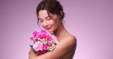 Gülümseyen beyaz bir kadın, rüya gibi bir stüdyo ortamında renkli bir buket pembe çiçeği kucaklıyor. Romantik, ilkbahar, sağlık ya da kadınsı yaşam tarzı içeriği için mükemmel..