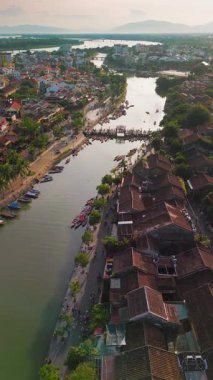 İnsansız hava aracı Hoi An, Vietnam 'ın yukarısında kademeli olarak göğe yükselir, nehir kenarını, köprüyü, çatıları ve uzak dağları güpegündüz tarar. Turizm, kültür ve...