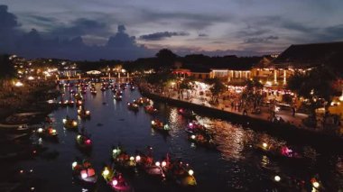 Hoi An 'ın alacakaranlıkta fenerle aydınlatılmış tekneleri ve hareketli rıhtım boyunca parlayan ışıkları olan sihirli bir drone görüntüsü. Kültür, turizm ve tanıtım medyası için ideal. 