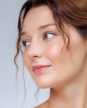 Kusursuz derisi ve minimum makyajı olan güzel bir genç kadının yüksek çözünürlüklü yakın çekimi. Nazik bir ifadeyle kameradan dışarı bakıyor. Gevşek saç telleri yüzünü çerçeveletip doğal ve...