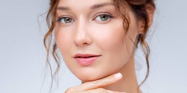 Kusursuz cilt ve yumuşak stüdyo ışığında doğal makyajı olan beyaz bir kadının özgüvenli portresi. Cilt bakımı, güzellik, sağlık ve kozmetik promosyonlar için ideal..