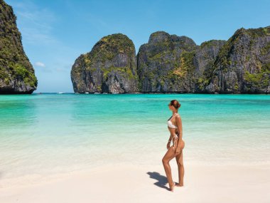 Maya Körfezi, Ko Phi Phi, Tayland kıyılarında beyaz bikinili genç bir kadın turkuaz deniz ve dramatik uçurumlara bakıyor. Seyahat, tatil ve tropikal yaşam tarzı görselleri için ideal.