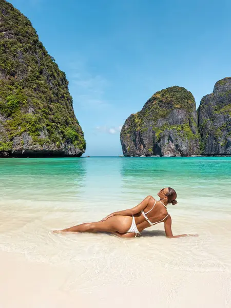 Maya Körfezi 'nin ikonik plajında uzanan beyaz bikinili genç bir kadının çarpıcı dikey kompozisyonu. Bereketli kireçtaşı kayalıkları ve kristal berrak turkuaz bir zemin üzerine kurulur.