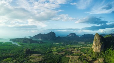 Khao Thong, Krabi, Tayland 'da tropikal tarım arazileri, yemyeşil verimli kayalıklar ve parlak mavi bir gökyüzü altında dramatik kireçtaşı kayalıkları olan güzel bir hava manzarası. Seyahat ve doğa kavramları için harika..