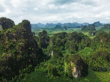 Krabis kireçtaşı tepeleri ve bulutlu gökyüzü ile tropikal orman manzarasının dramatik hava görüntüsü. Çevre seyahatleri, doğa afişleri, çevre kampanyaları ve macera promosyonları için mükemmel..