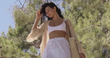 Hafif yaz kıyafetleri içinde trend bir kadın bir uçurumun kenarında duruyor, denize doğru bakıyor. Moda, yaşam tarzı, sağlık ve seyahat temalı içerik için ideal bir yavaş çekim sahnesi.