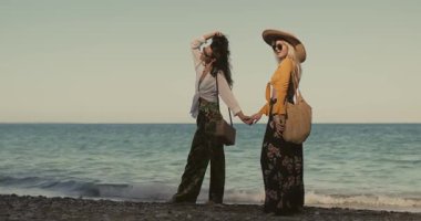 Çiçekli pantolonlu ve şık bluzlu en iyi arkadaşlar sevinçten kollarını kaldırıyorlar. Arkadaşlık, moda, yaşam tarzı ve seyahat promosyonları için mükemmel bir yavaş çekim sahnesi..