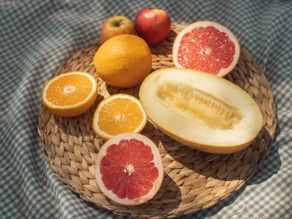 Hasır bir tabakta karpuz, portakal ve elma gibi çeşitli taze meyveler sergilenmektedir. Yaz pikniklerini ve sağlıklı beslenmeyi teşvik etmek için ideal, doğal güzelliği ve cazibesini vurgulamak için.