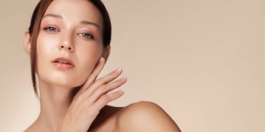 Yüzüne hafifçe dokunan parlak tenli beyaz bir kadının zarif stüdyo portresi. Cilt bakımı, vücut bakımı, el kremi, yüz bakımı ve sağlık promosyonları için mükemmel..