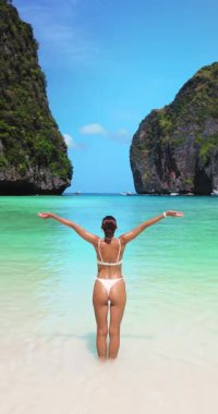 Tayland 'ın Maya Körfezi' nde, turkuaz sularda kollarını kaldıran neşeli beyaz bir kadının arka görüntüsü. Seyahat, özgürlük, güzellik ve yaz yaşam tarzı için yavaş çekim dikey video konsepti.