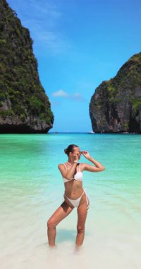 Modayı takip eden kadın model, Krabi, Maya Körfezi sahilinde kendine güvenen beyaz bir bikini giyiyor. Tropik ortam, güzellik, yaz, seyahat, moda ve lüks promosyon içeriği için ideal.