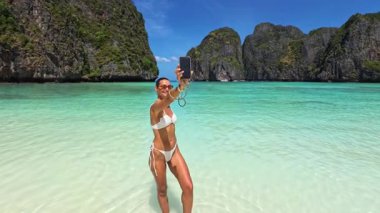 Beyaz bikinili beyaz bir kadın Maya Körfezi, Tayland 'da akıllı telefonuyla selfie çekiyor. Lüks seyahat, yaz, tropik cennet ortamında nüfuz sahibi ve dijital yaşam tarzı tanıtım konsepti.
