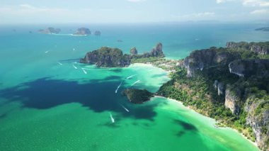 Railay Sahili, Krabi 'nin insansız hava aracı görüntüleri canlı mavi deniz, verimli kayalıklar ve turist tekneleri gösteriyor. Çarpıcı bir tropikal konsept, seyahat tanıtımları ve hedef pazarlama için mükemmel..