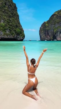 Tayland 'da Maya Körfezi' nde diz çökerken bikinili neşeli kadının dikey ağır çekimleri. Tropikal geziler, tatil beldeleri ve yaz moda tanıtımları için harika..