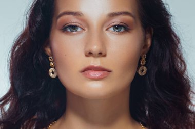 Parlak derili, parlak dudaklı ve yuvarlak altın küpeli genç bir kadının stüdyo güzelliği. Lüks kozmetik ürünleri, cilt bakımı promosyonları ve moda yazıları için ideal..