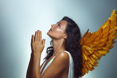 Beyaz Yunan elbiseli zarif beyaz kadın, altın melek kanatları ve dua eden eller. Yazı işleri ve tanıtım kullanımı için umut, inanç ve fanteziyi sembolize eden kavramsal güzellik fotoğrafı.