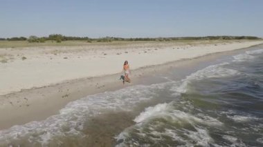 Mayo giymiş genç bir kadının ıssız bir plajda huzur içinde yürüdüğünü gösteren drone görüntüleri. Seyahat, yaşam tarzı, tanıtım ve yaz temalı projeler için ideal kavramsal ve manzaralı stok videosu.
