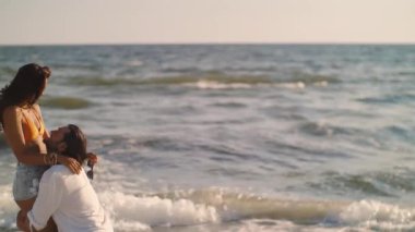 Kumsalda romantik bir çift ağır çekimde, kadını su kenarından tutan adamla. Seyahat promosyonları, romantik plaj temalı görseller ve yüksek kaliteli yaşam tarzı için ideal.