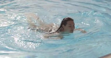 Leopar mayo giymiş genç bir kadın açık mavi bir havuzdan ıslak saçlar ve parlak bir ciltle çıkar. Yavaş çekim yaşam tarzı, seyahat, moda ve cilt tanıtımı için ideal..