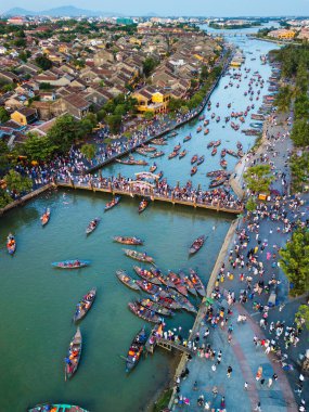 Hoi An 'ın ikonik köprüsünün canlı bir insansız hava aracı fotoğrafı aşağıda yüzen fener tekneleriyle dolu. Afişler, başyazılar ve seyahat reklamları için mükemmel bir kültür ve turizm çekimi.