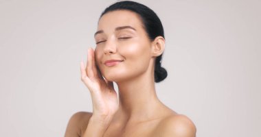 Yüzüne nazikçe dokunan, parlak tenli ve huzurlu bir ifadeyle beyaz bir kadının yüksek çözünürlüklü portresi. Güzellik markaları, sağlık reklamları ve cilt bakımı için mükemmel..