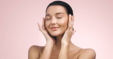 Pembe arka planda, pürüzsüz, parlak bir teni ve minimum makyajı olan genç bir kadının zarif portresi. Temiz güzellik, cilt ürünleri reklamları ve sağlıklı görünüm için mükemmel..