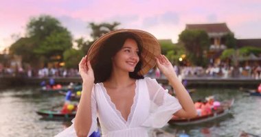 Beyaz elbiseli, koni şapkalı genç Asyalı kadın Hoi An, Vietnam 'da gün batımında gülümsüyor. Güneydoğu Asya 'da kültür, güzellik ve miras turizminin kavramsal seyahat tanıtımı.