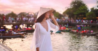 Beyaz elbiseli ve konik şapkalı zarif Asyalı kadın gün batımında nehre bakıyor. Popüler bir turizm beldesi, seyahat tanıtımı, moda ve yaşam tarzı içeriği için ideal..