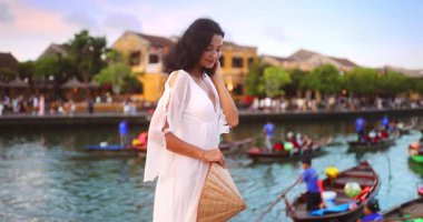 Hoi An 'ın eski kasabasında beyaz elbiseli ve geleneksel şapkalı şık Asyalı kadın modeller su kenarında poz veriyor. Kültürel zarafetle kavramsal turizm ve moda tanıtımı.