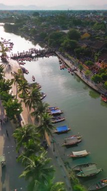 Hoi An nehri boyunca demirlemiş teknelerin parlak dikey hava görüntüleri, Vietnam. Seyahat, turizm, kültür ve manzaralı şehir yaşam tarzı promosyonları için yüksek kaliteli konsept video.