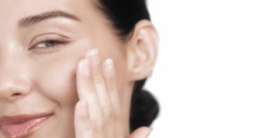 Işıl ışıl gülümseyen ve yüzüne nazikçe dokunan genç bir kadının yakın çekimi. Parlak ve sağlıklı bir ten. Cilt bakımını, sağlığını ve doğal ışıltı ve benlik odaklı güzellik ürünlerini teşvik etmek için mükemmel.