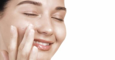 Parlak tenli ve parlak gözlü, yanağa dokunan gülümseyen bir kadının aşırı yakın çekimi. Güzellik markası reklamları, cilt bakımı, yüz bakımı ve sağlık promosyon malzemeleri için mükemmel..