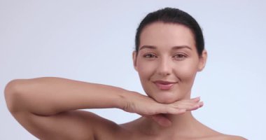 Neşeli beyaz kadın, elleri çenesinin altında ve beyaz arka planda yumuşak bir gülümsemeyle poz veriyor. Güzellik, yaşam tarzı, cilt bakımı, yüz bakımı, kozmetik ve sağlık reklamları için ideal.