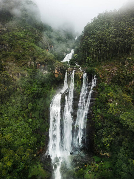 Вид с воздуха на Влюблённых Прыгающий Водопад в Нувара-Элия, Шри-Ланка, стекающий вниз по туманным скалам через густые джунгли. Идеально подходит для рекламы путешествий, экологических акций и экотуризма.