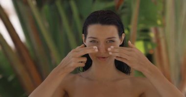 Zenginleştirilmiş güzellik modeli verimli bir tropikal ortamda güneş ışığı altında krem sürüyor. Moda cilt bandı konsepti kozmetik reklamlar, sağlık ve parlayan cilt içeriği için mükemmel.