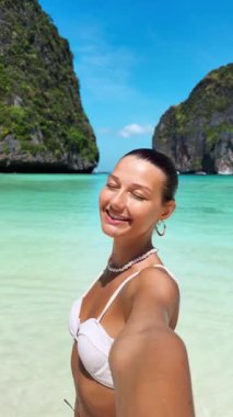 Tayland 'da Maya Körfezi sahilinde selfie çeken mutlu bir kadının dikey ağır çekimi. Etkilendirici içerik, seyahat pazarlaması ve tropikal yaşam tarzı tanıtımları için harika..