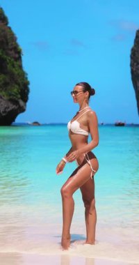 Beyaz bikinili beyaz kadın güneş gözlüklerini parlak tropikal güneşin altında ayarlıyor. Tayland 'da Maya Körfezi sahilinde çekilen bu kavramsal çekim lüks seyahat, güzellik ve tarz tanıtımlarına uygundur..