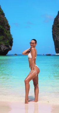 Bronzlaşmış kadın model Tayland 'daki Maya Körfezi plajında güven içinde poz veriyor. Kristal berrak su ve egzotik uçurumlar lüks moda, sağlık ve seyahat videoları için ideal hale getirir..