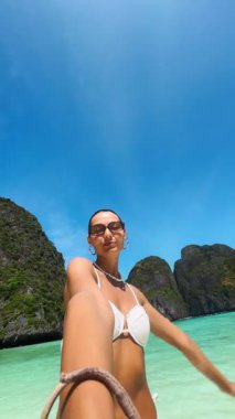 Gülümseyen kadın etkili Maya Körfezi, Koh Phi Phi, Tayland 'da beyaz bikinili selfie anları yakalıyor. Seyahat, moda ve yaşam tarzı kampanyaları için yüksek kaliteli bir dikey video.