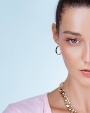 Çıplak, parlak dudakları, halka küpeleri ve altın bir kolyesi olan genç bir kadının yüzünün yarısını gösteren minimalist moda portresi. Editör, güzellik veya mücevher pazarlama içeriği için harika.