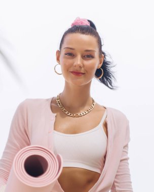 Kendine güvenen genç bir kadının elinde pembe yoga minderiyle sahile yakın bir sağlık seansı için hazır. Günlük kıyafetlerle, spor, sağlık ve pozitif enerjiyi somutlaştırıyor. Sağlık için ideal.