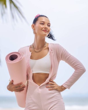 Pembe yoga minderini tutarken kendine güvenen şık, genç beyaz bir kadın, şık bir aktivite kıyafeti giyiyor, sağlık promosyonları, fitness reklamları ve sağlıklı yaşam tarzı temaları için mükemmel..