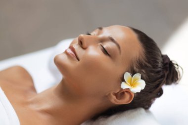 Beyaz bir kadın, saçlarında çiçekler ve beyaz bir havlunun üzerinde uzanan parlak cildiyle huzurlu bir spa anından zevk alır. Cilt bakımı, güzellik, sağlık ve lüks geri çekilme malzemeleri için mükemmel..